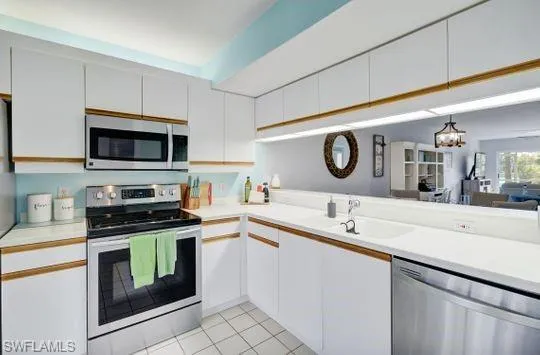 White cabinetry with wood-finish trim, stainless steel appliances, and a white sink
