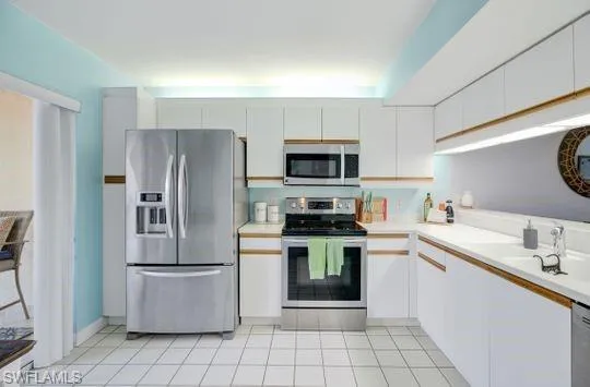Stainless steel appliances, white cabinetry with wood trim, white countertops, tile flooring, and a built-in microwave