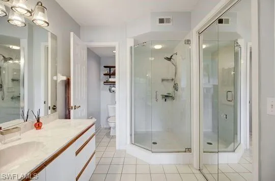 Spacious bathroom featuring a double glass-enclosed shower, single vanity with a solid surface countertop, and white tile flooring