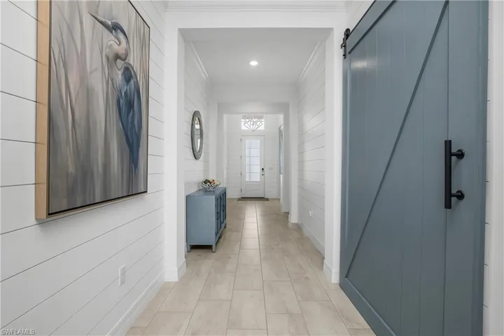 Entry hall is accented with glass door with transom window, crown molding, shiplap, and barn door leading to the HUGE office!