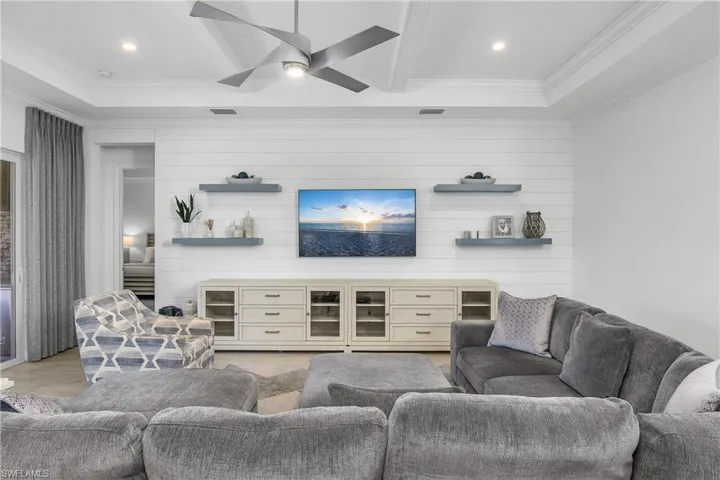 Spacious and open great room includes feature wall with shiplap and floating shelves, and tray ceilings with crown molding detail.