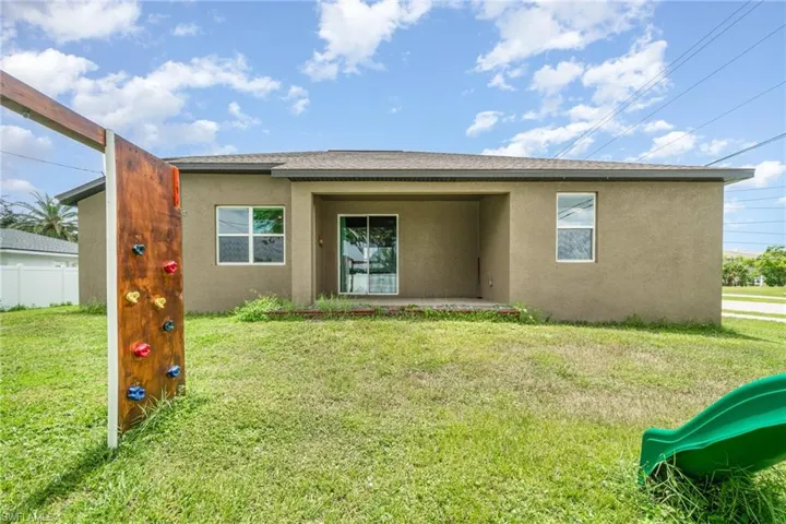 Rear view of house with stucco siding, a lawn, and a patio area