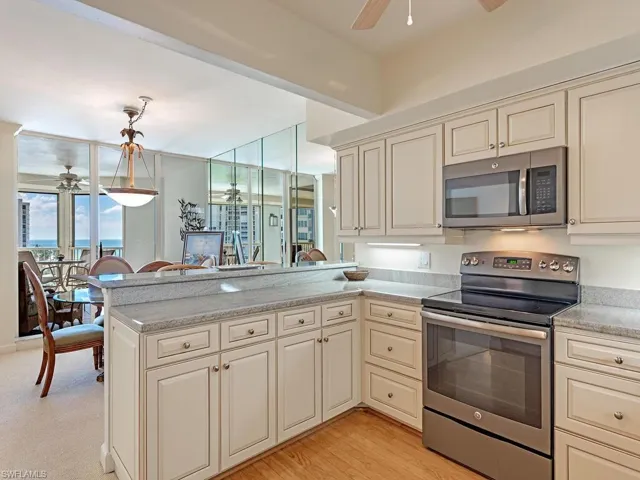 Kitchen with cream cabinets, ceiling fan, appliances with stainless steel finishes, light stone counters, and a peninsula