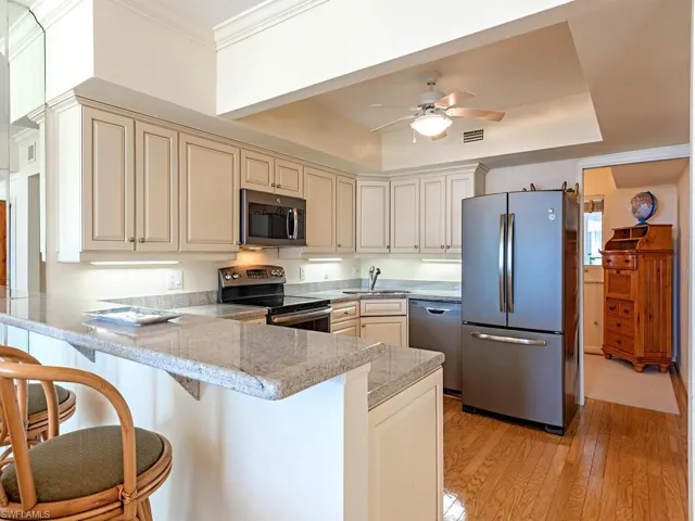 Kitchen with cream cabinetry, appliances with stainless steel finishes, a peninsula, light wood-style flooring, and a kitchen bar