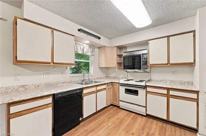 Kitchen featuring wood-finish flooring, white cabinetry with wood trim, and a double basin sink
