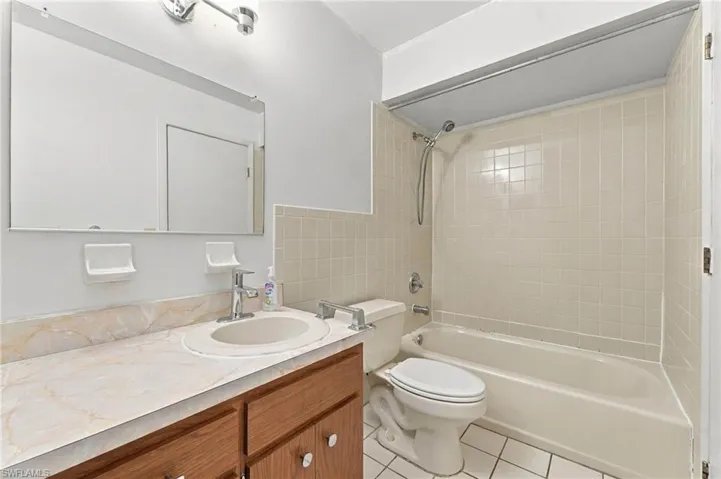 Bathroom featuring a vanity with an integrated sink, a large mirror, a tiled shower/tub combination, and tiled flooring