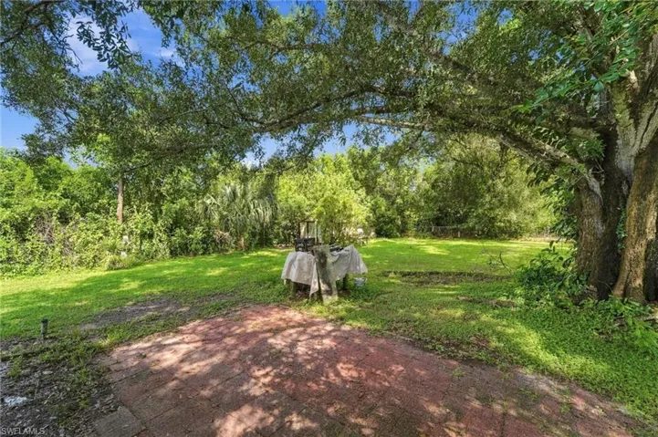 Expansive green lawn surrounded by mature trees, featuring a red brick patio