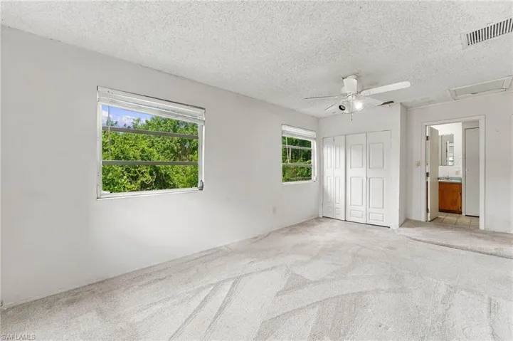 Carpeted flooring, two horizontal windows, white bi-fold closet doors, and a ceiling fan with integrated lighting