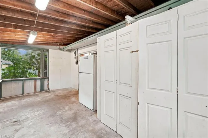 Concrete flooring with exposed wood beam ceiling, featuring a large window and white paneled storage units