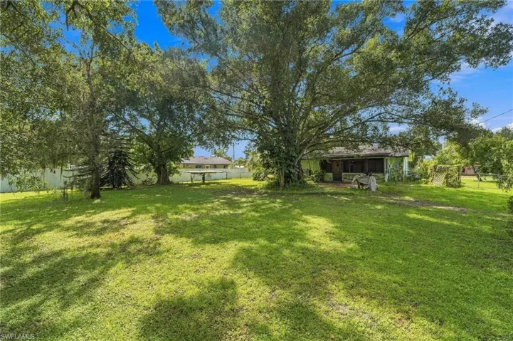 Expansive yard featuring mature trees, a manicured lawn, and a white perimeter fence