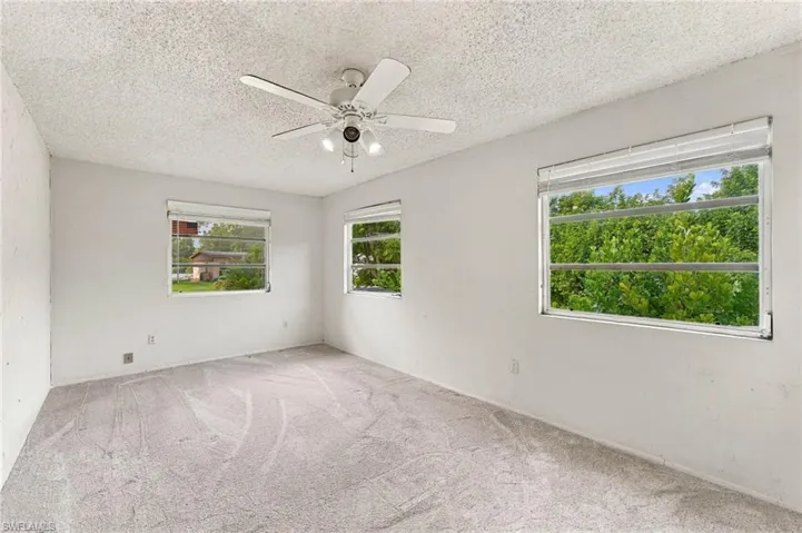 Textured ceiling, ceiling fan with integrated lighting, multiple windows, light-colored carpeting, white wall finishes