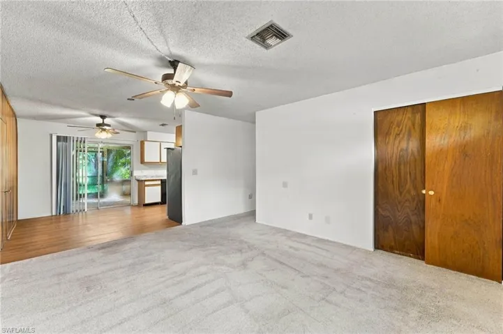Carpeted living area with two ceiling fans, wood-finish flooring, sliding glass doors, and a partial kitchen with white cabinetry