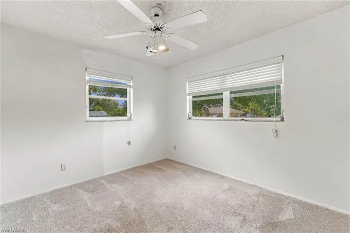 Light-colored carpeted flooring, white painted walls, and two windows with horizontal blinds