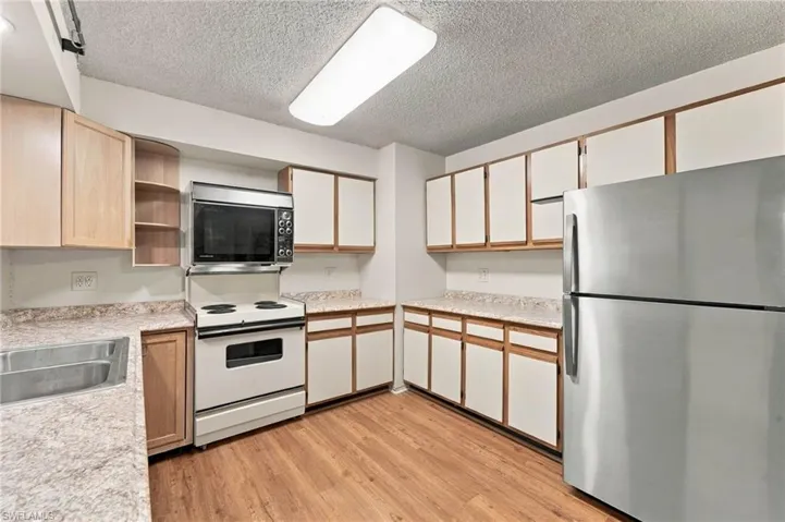 Galley kitchen featuring wood-finish flooring, ample cabinetry, stainless steel sink, and white appliances