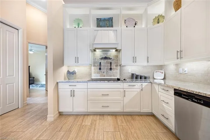 Kitchen featuring white cabinetry, crown molding, backsplash, stainless steel dishwasher, and light stone countertops