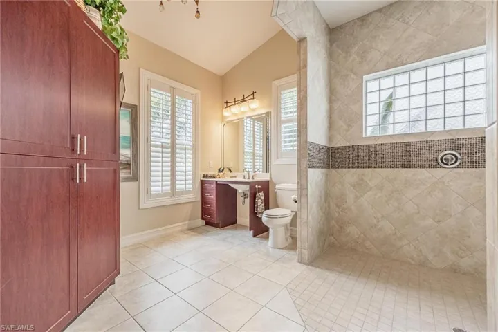 Bathroom featuring vaulted ceiling, vanity, tile patterned flooring, and toilet