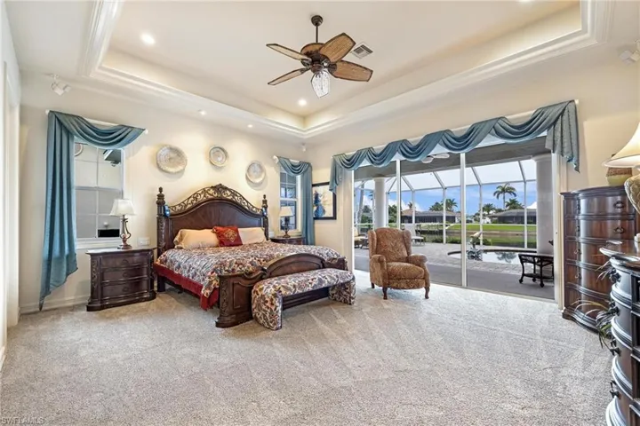 Carpeted bedroom with ceiling fan, access to exterior, and a tray ceiling