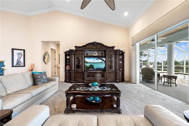 Living room with crown molding, vaulted ceiling, carpet, and ceiling fan