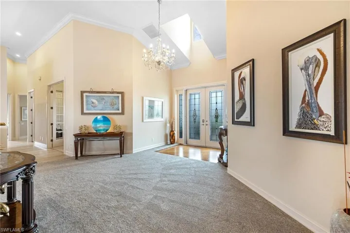 Carpeted entryway featuring an inviting chandelier, high vaulted ceiling, crown molding, and french doors