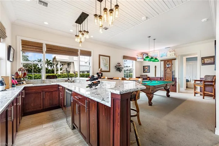 Kitchen featuring light colored carpet, light stone countertops, decorative light fixtures, and pool table