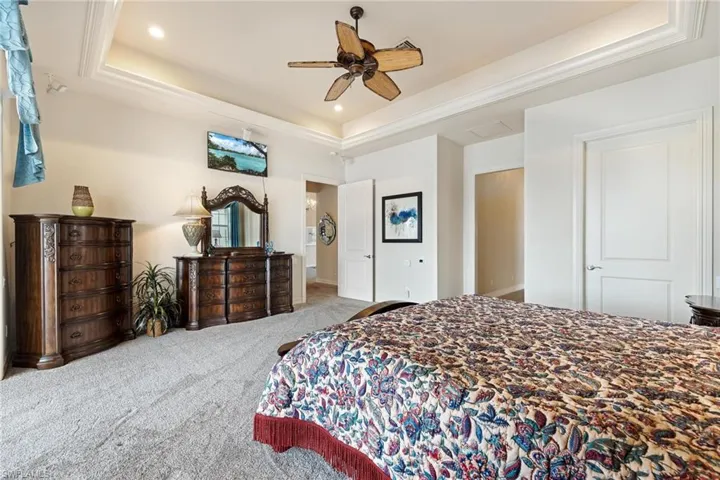 Carpeted bedroom featuring ceiling fan and a raised ceiling