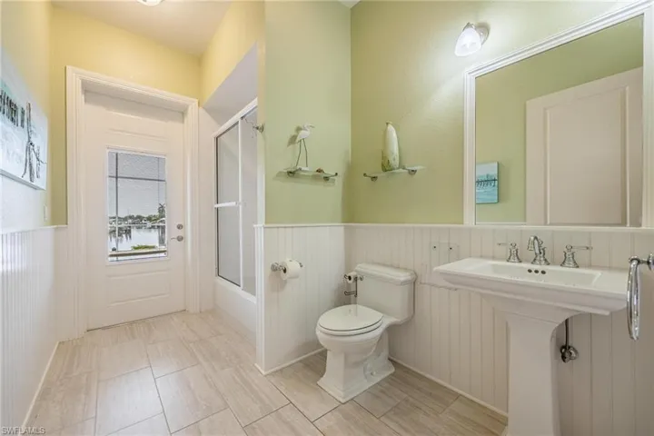 Bathroom with combined bath / shower with glass door, tile patterned flooring, and toilet