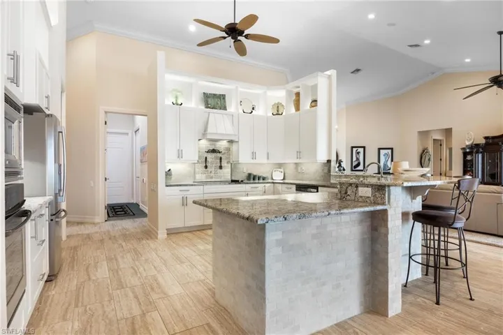 Kitchen featuring white cabinetry, custom range hood, a breakfast bar, ceiling fan, and light stone countertops