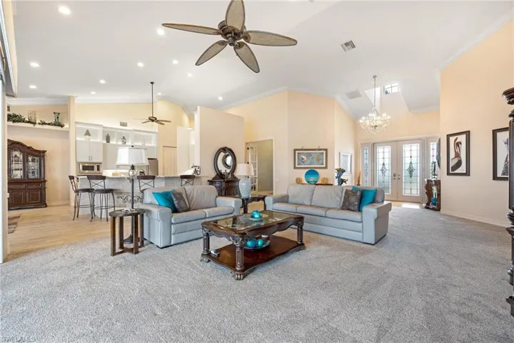 Living room with ceiling fan with notable chandelier, light colored carpet, and ornamental molding