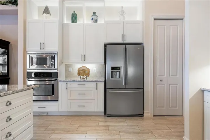 Kitchen with decorative backsplash, light stone counters, appliances with stainless steel finishes, and white cabinets