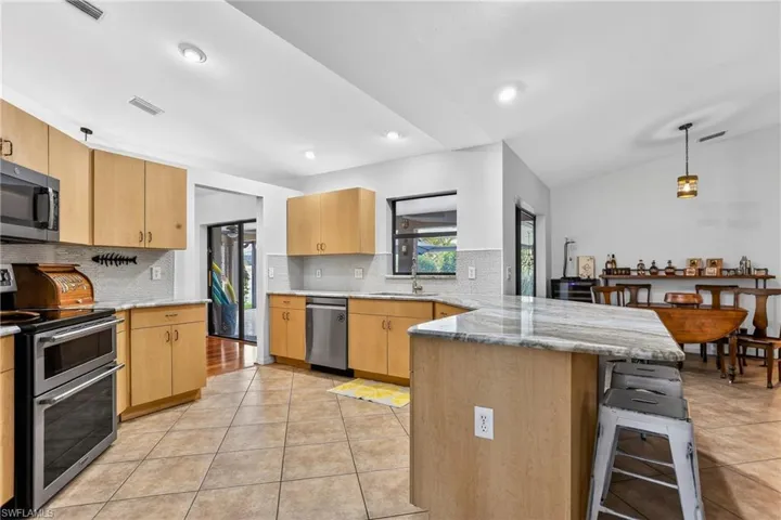 Kitchen with a peninsula, stainless steel appliances, a breakfast bar area, light granite countertops, and backsplash