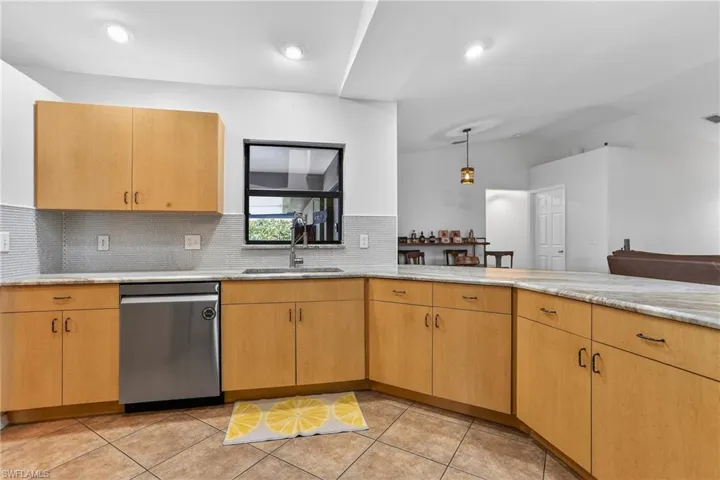 Kitchen featuring stainless steel dishwasher, a peninsula, light tile  flooring, decorative backsplash, and vaulted ceiling