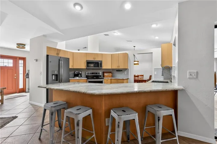 Kitchen with breakfast bar, tasteful backsplash, light granite countertops, and vaulted ceiling