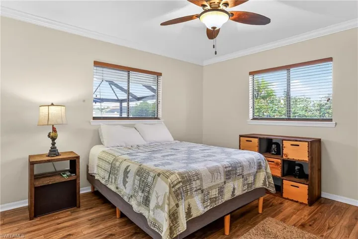 Bedroom featuring laminate floors, crown molding, multiple windows, and a ceiling fan