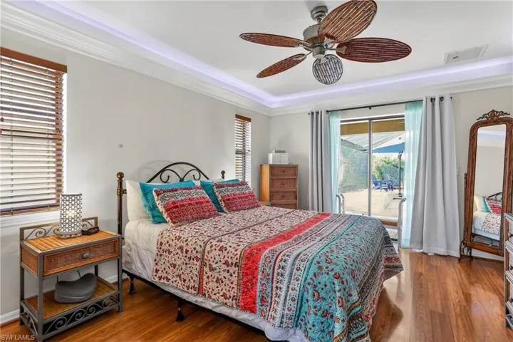 Bedroom with laminate floors access to outside, a ceiling fan, and a tray ceilingwith mood lighting