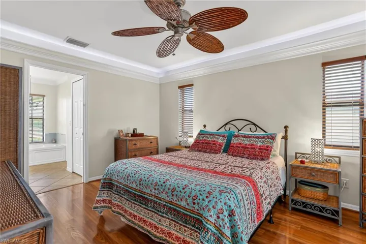 Bedroom featuring laminate floors, a ceiling fan, ensuite bathroom, and crown molding