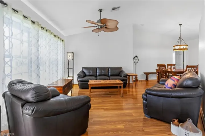 Living area featuring lofted ceiling, laminate floors, healthy amount of natural light, ceiling fan
