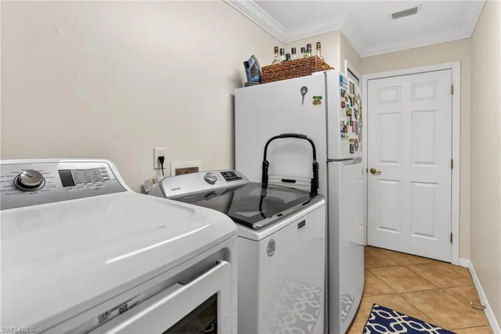 Laundry area with crown molding,  tile floors, and washing machine and clothes dryer