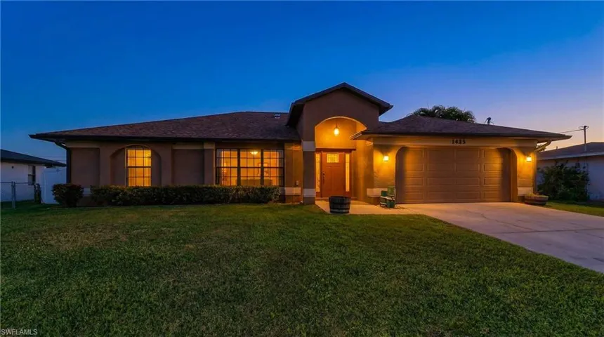 View of front of property featuring an attached garage, stucco siding, driveway, and a front yard