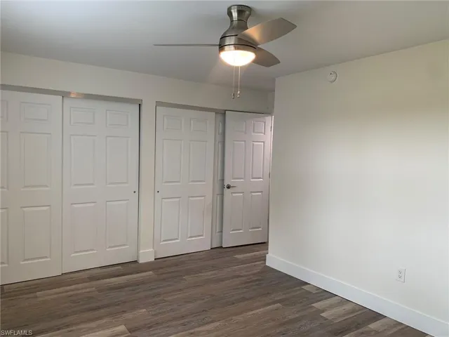 Unfurnished bedroom featuring dark wood finished floors, two closets, and a ceiling fan