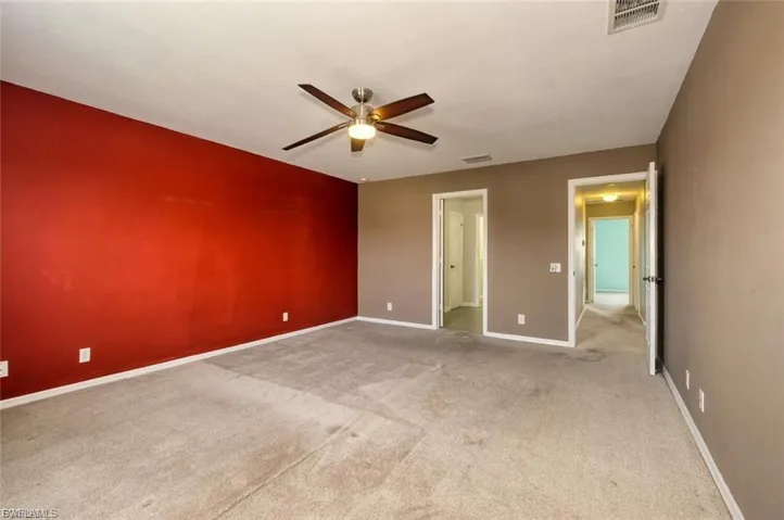 Spacious room featuring carpeting, a ceiling fan with integrated lighting, and a bold accent wall