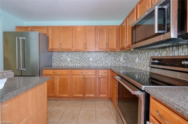 Kitchen featuring wood cabinetry, stainless steel appliances, speckled countertops, a mosaic tile backsplash, and tile flooring
