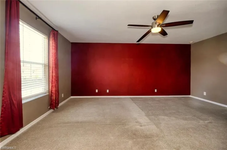 Spacious room featuring carpeting, a red accent wall, and a ceiling fan with integrated lighting