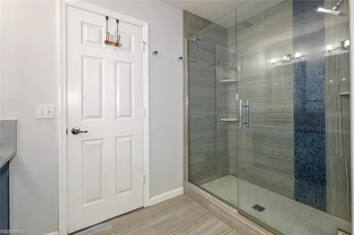 Glass-enclosed shower featuring striped wall tile with an accent mosaic panel, built-in shelving, and a rain showerhead