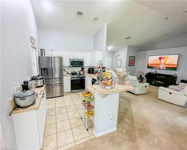 Kitchen with white cabinetry, light carpet, stainless steel appliances, a kitchen breakfast bar, and high vaulted ceiling