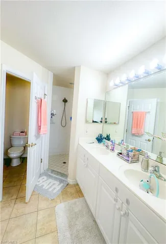 Bathroom with double vanity, tile patterned flooring, toilet, and tiled shower