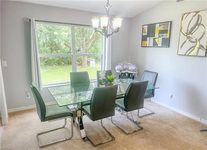 Carpeted dining space featuring an inviting chandelier, lofted ceiling, and plenty of natural light