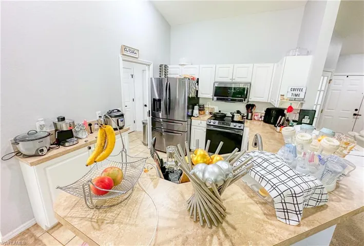 Kitchen with white cabinetry, light tile patterned flooring, high vaulted ceiling, and stainless steel appliances
