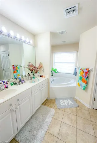 Bathroom with tiled tub, tile patterned floors, and double sink vanity