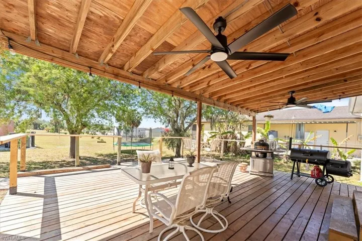 Wooden deck with outdoor dining area, a trampoline, area for grilling, and ceiling fan