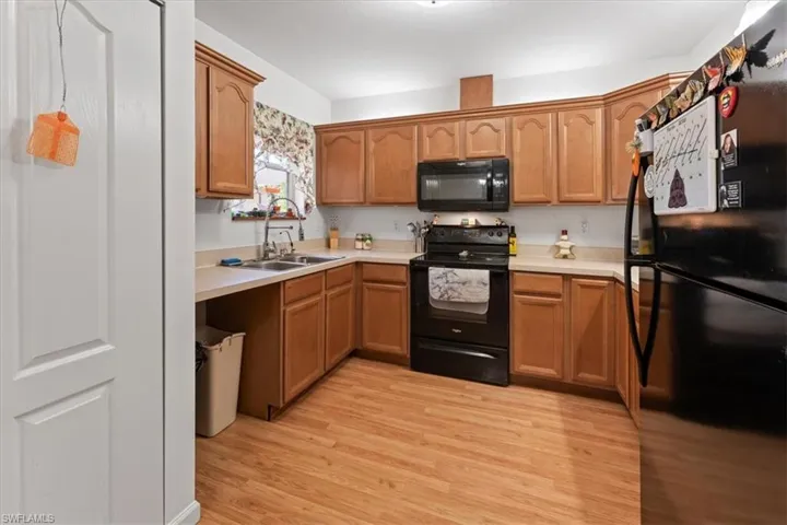 Kitchen with light wood finished floors, light countertops, brown cabinets, black appliances, and a sink
